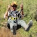 A smiling Guest holds the lanyard of the zip line trolley as he rides along above brush filled terrain
